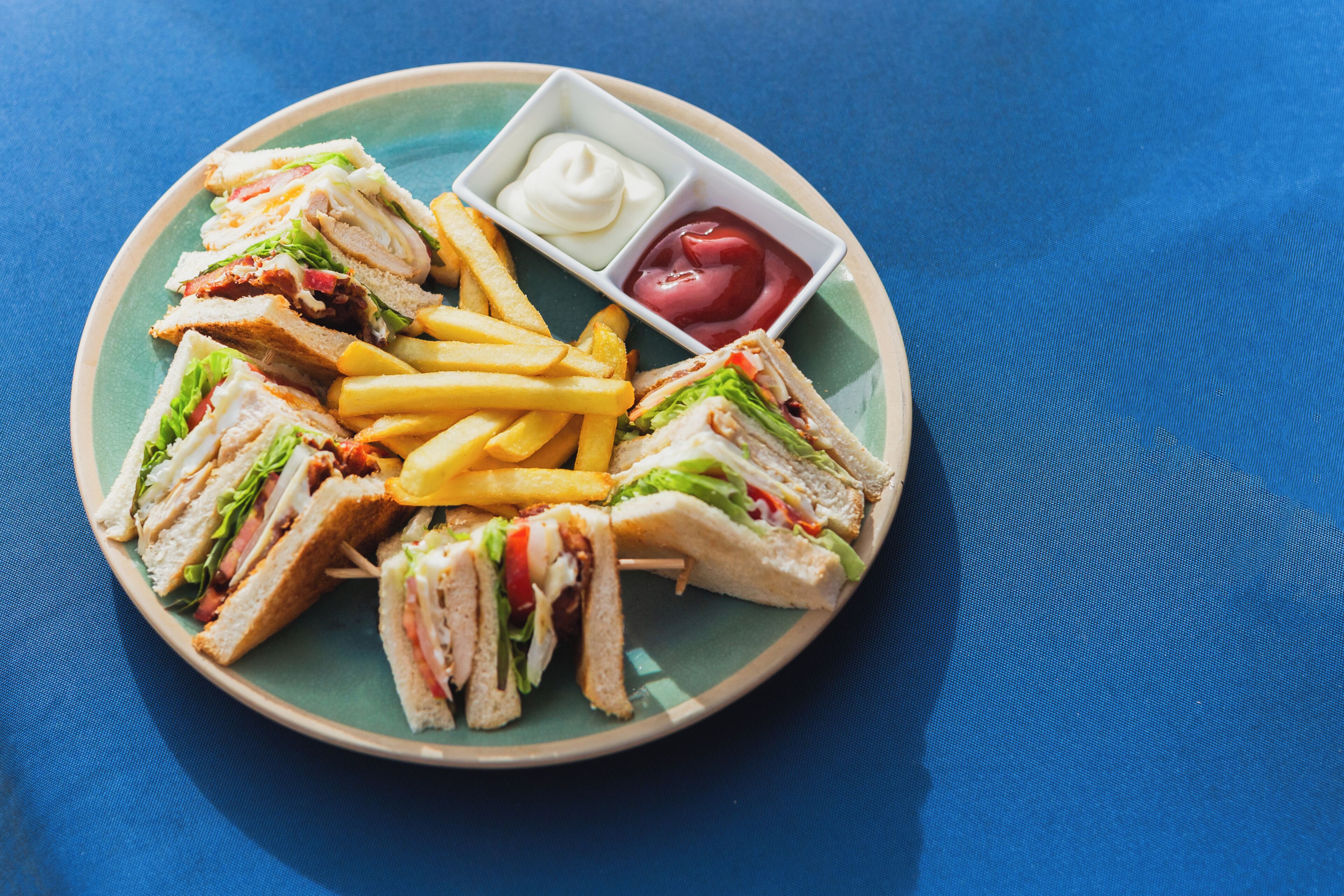 Un plato con sándwiches, papas fritas y dos salsas.