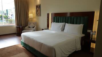Una habitación de hotel con una cama grande, una silla, una mesita de noche y una ventana con cortinas.