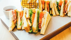 A tray with several sandwiches cut into triangles, a small bowl of sauce, and a basket with bananas.