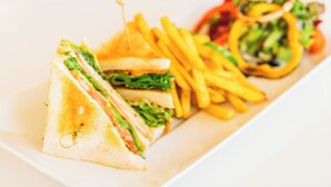 A sandwich cut in half with a toothpick, next to a plate of French fries and a salad with a slice of tomato.