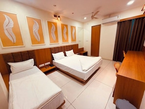 Een hotelkamer met twee bedden, een houten hoofdeinde, een bureau en een groot raam met gordijnen.
