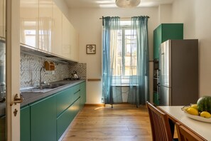 Eine Küche mit türkis-blauen Schränken, einem Edelstahl-Kühlschrank und einem Holzespeisetisch mit einer Obstschale.