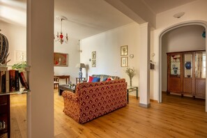 Ein Wohnzimmer mit einem gemusterten Sofa, einem Esstisch und einer Chandelüster.