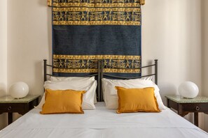 Ein Doppelbett mit weißen Bettwäsche und zwei senfgelben Kissen, an beiden Seiten umrahmt von Nachttischen mit weißen Lampen.