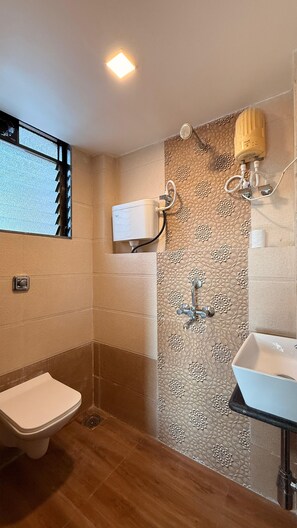 A bathroom with a toilet, a shower with a wall-mounted heater, and a sink.