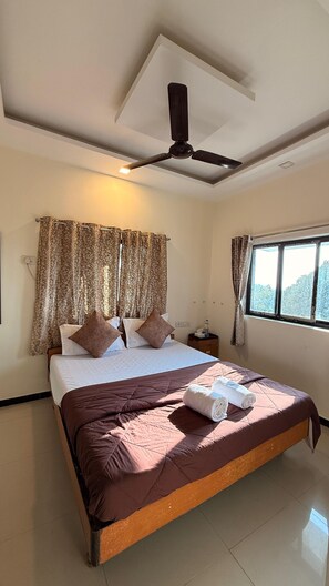 A hotel room with a bed, a ceiling fan, curtains, a window, and a nightstand with a bottle.