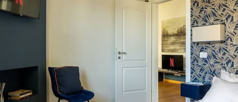 A hotel room with a bed, a chair, a TV, and a door leading to another room.