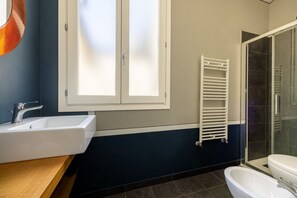 A bathroom with a white sink, a mirror, a towel rack, a shower area, and a toilet. - The Nerli Edit by Maison Florence (Florence)