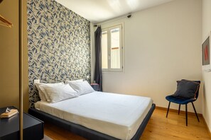 A bedroom with a bed, a chair, a nightstand, and a window. - The Nerli Edit by Maison Florence (Florence)