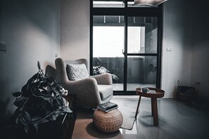 Een moderne woonkamer met een grote schuifpui naar een buitenruimte, een comfortabele fauteuil, een klein rond tafeltje en een potplant.