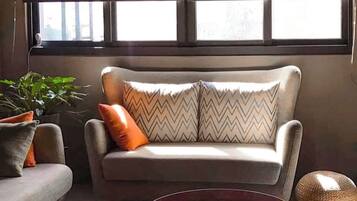 A living room with a sofa, two armchairs, a round coffee table, and a large window with blinds.
