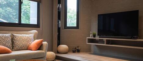 A modern living room with a sofa, a coffee table, a television, and a window with a view of trees.