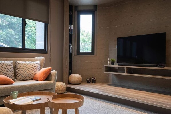 Una sala de estar moderna con un sofá, una mesa de centro, un televisor y una ventana con vistas a árboles.