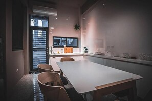 Een moderne keuken met een groot schiereiland, een eethoek met tafel en stoelen, en een raam met zonwering.