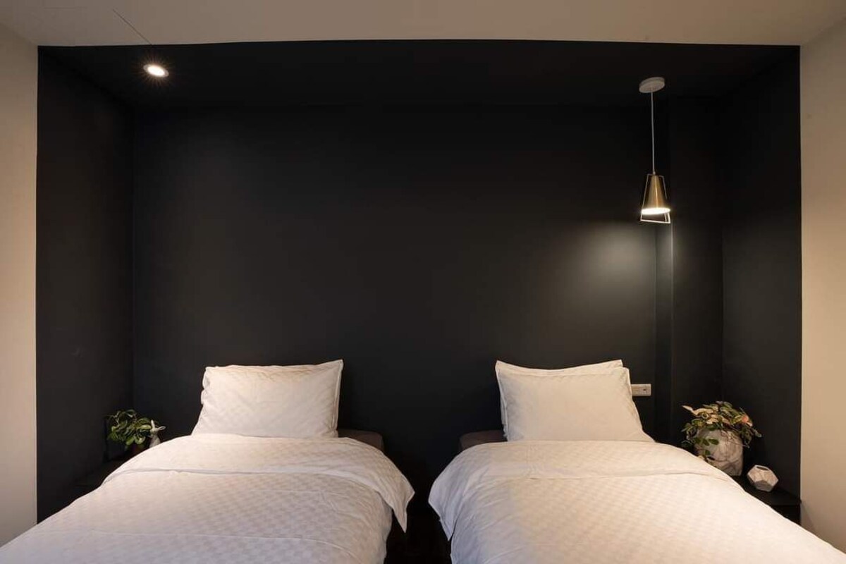 Een kamer met twee bedden, een donkere muur en een hanglamp.