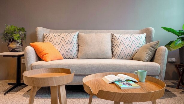 Un salon moderne avec un canapé gris, deux petites tables d’appoint en bois et un livre posé sur l’une des tables.