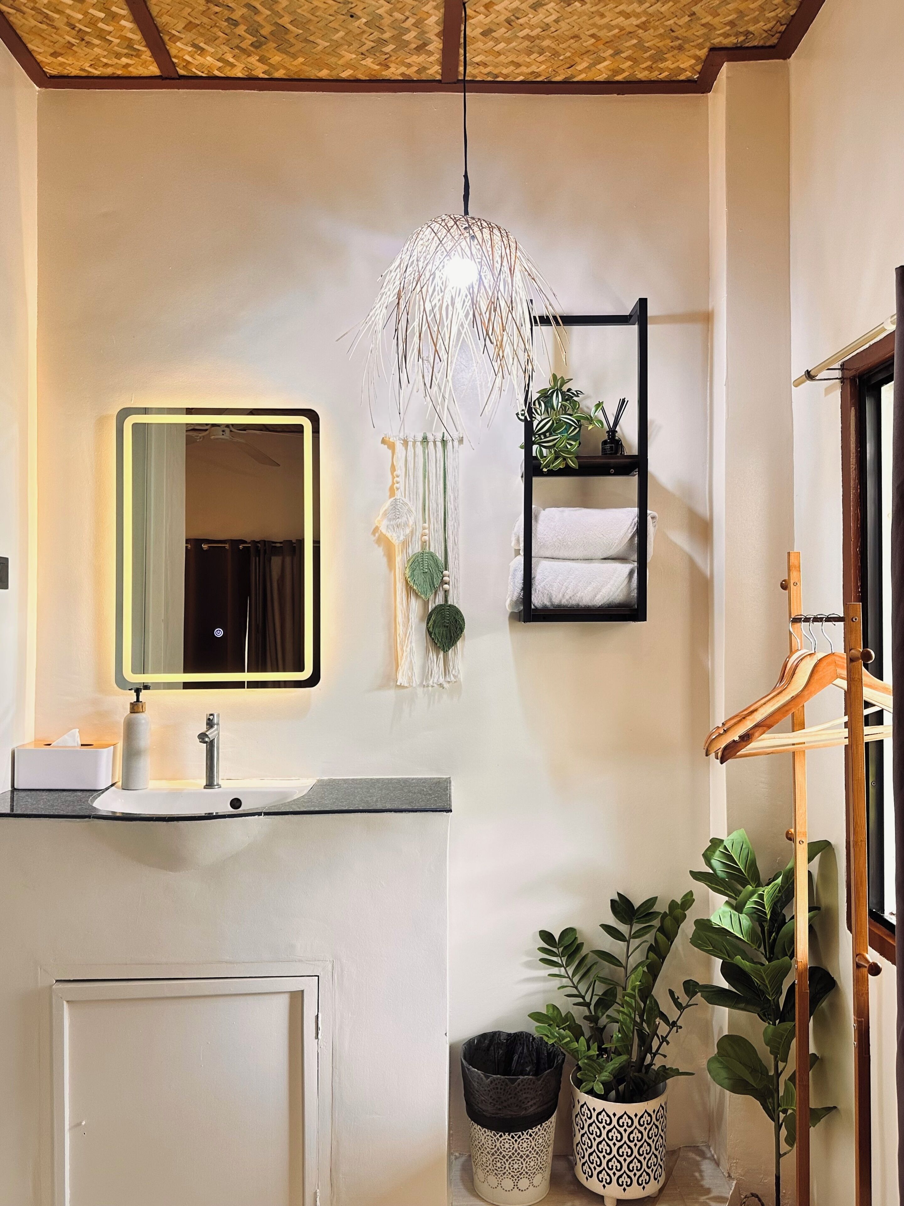 Een badkamer met een wastafel, spiegel, macramé lamp en een handdoekrek.