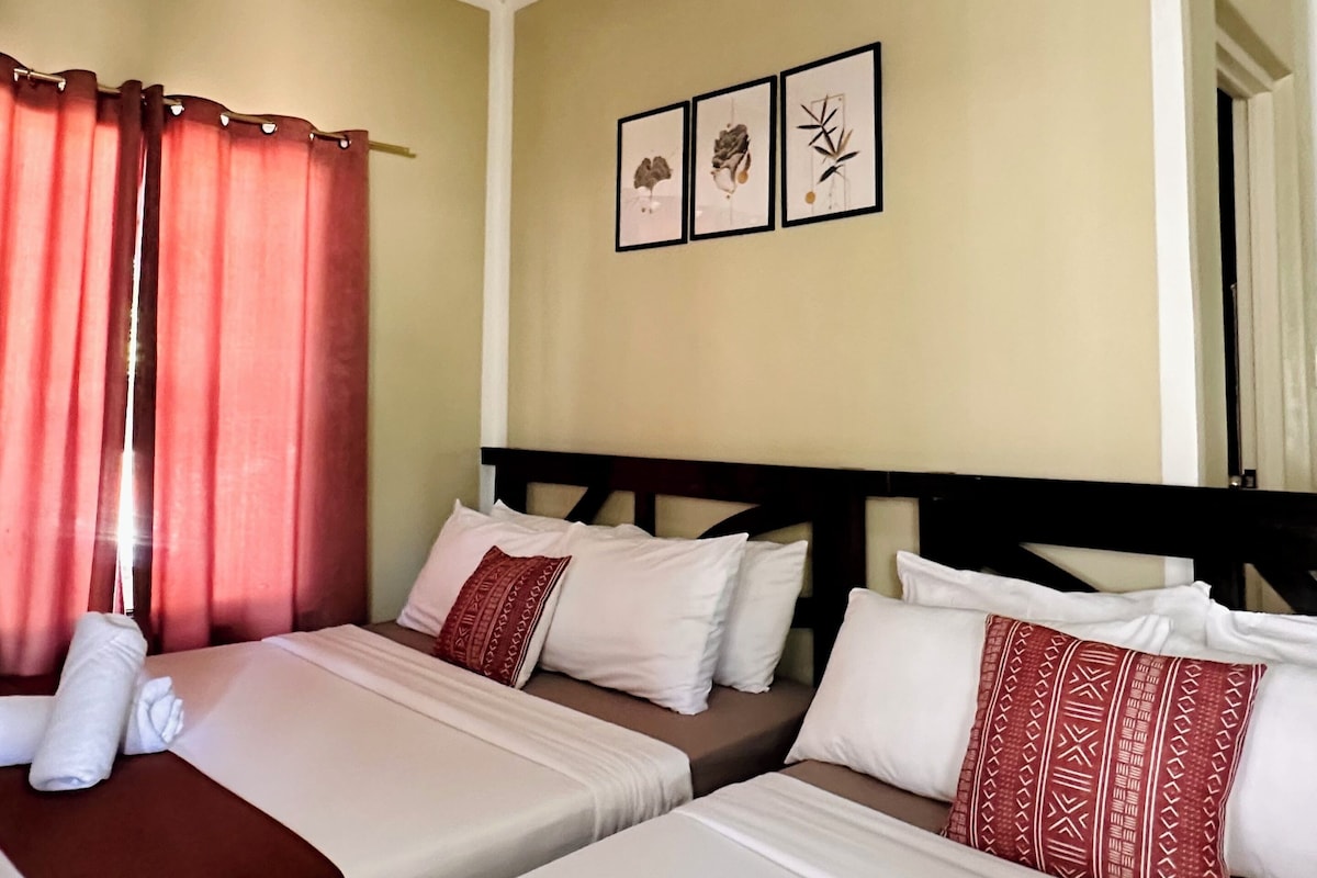 A hotel room with two beds, a ceiling fan, and three framed pictures on the wall.