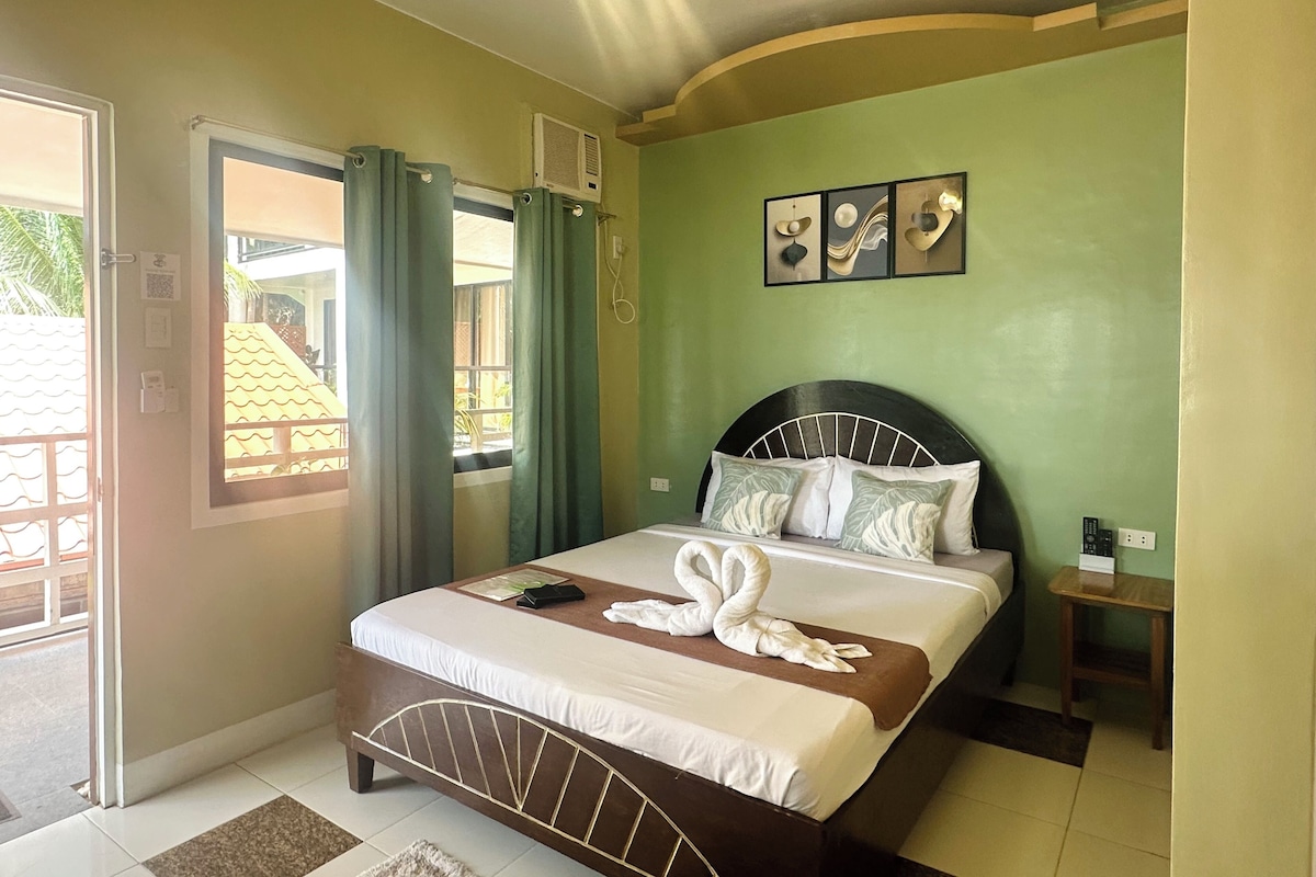A hotel room with a bed, a ceiling fan, a window with curtains, and a wall-mounted air conditioner.