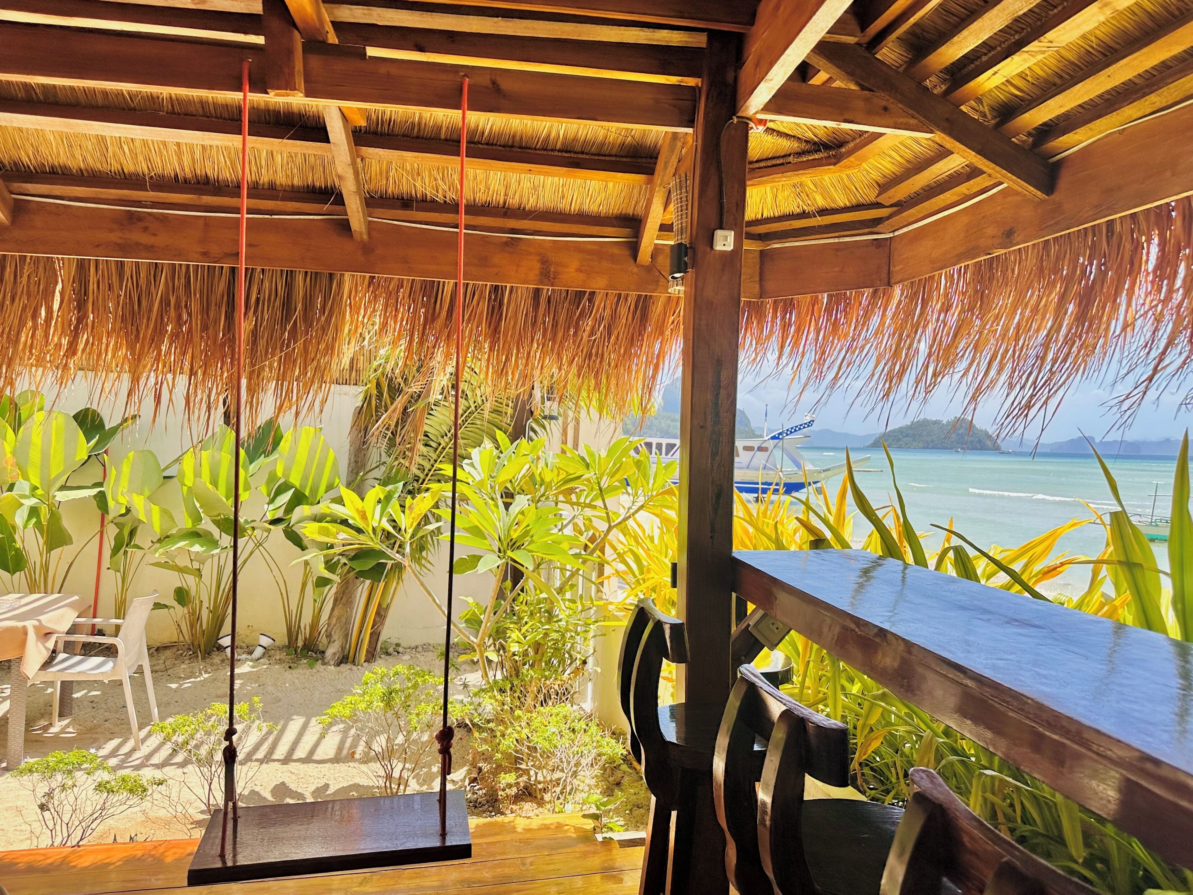 A wooden deck with a thatched roof, a swing, and a view of the ocean.