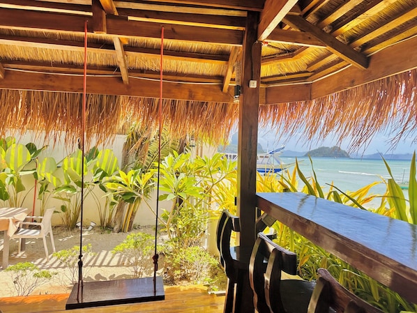 A wooden deck with a thatched roof, a swing, and a view of the ocean.