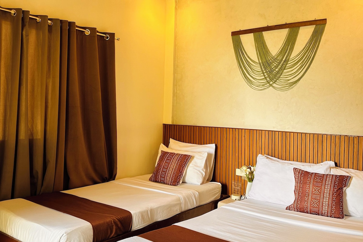Habitación de hotel con dos camas, ventilador de techo, techo tejido y un adorno en la pared.
