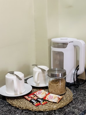 En kaffemaskine, to hvide kopper, en kaffekande og portioner kaffemælk på en køkkenbordplade.