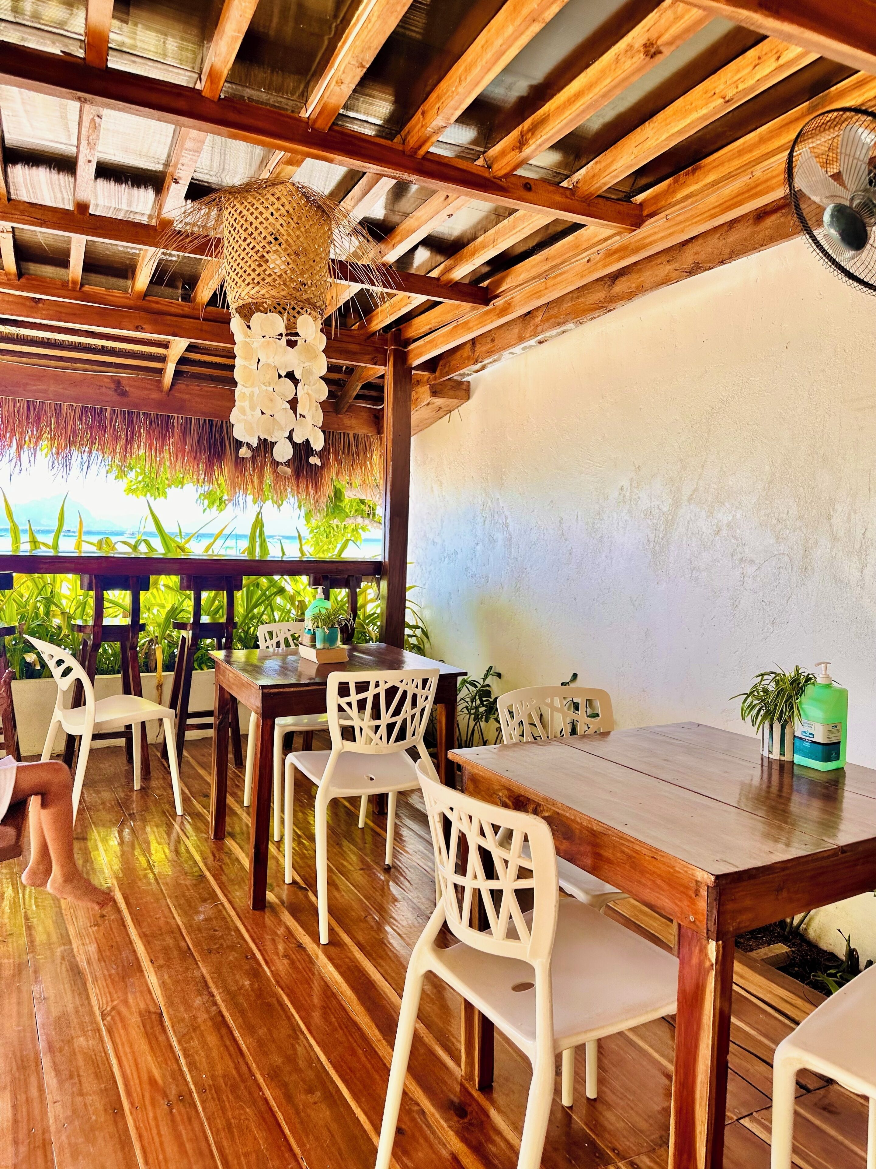 A wooden dining area with a thatched ceiling, white plastic chairs, and a wooden table.
