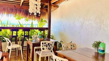 A wooden dining area with a thatched ceiling, white plastic chairs, and a wooden table.