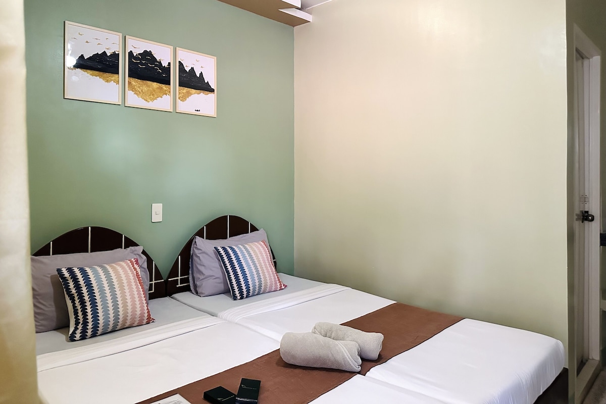 A double bed with two pillows, a brown blanket, and a pair of slippers on the floor. There are two framed pictures on the wall above the bed.