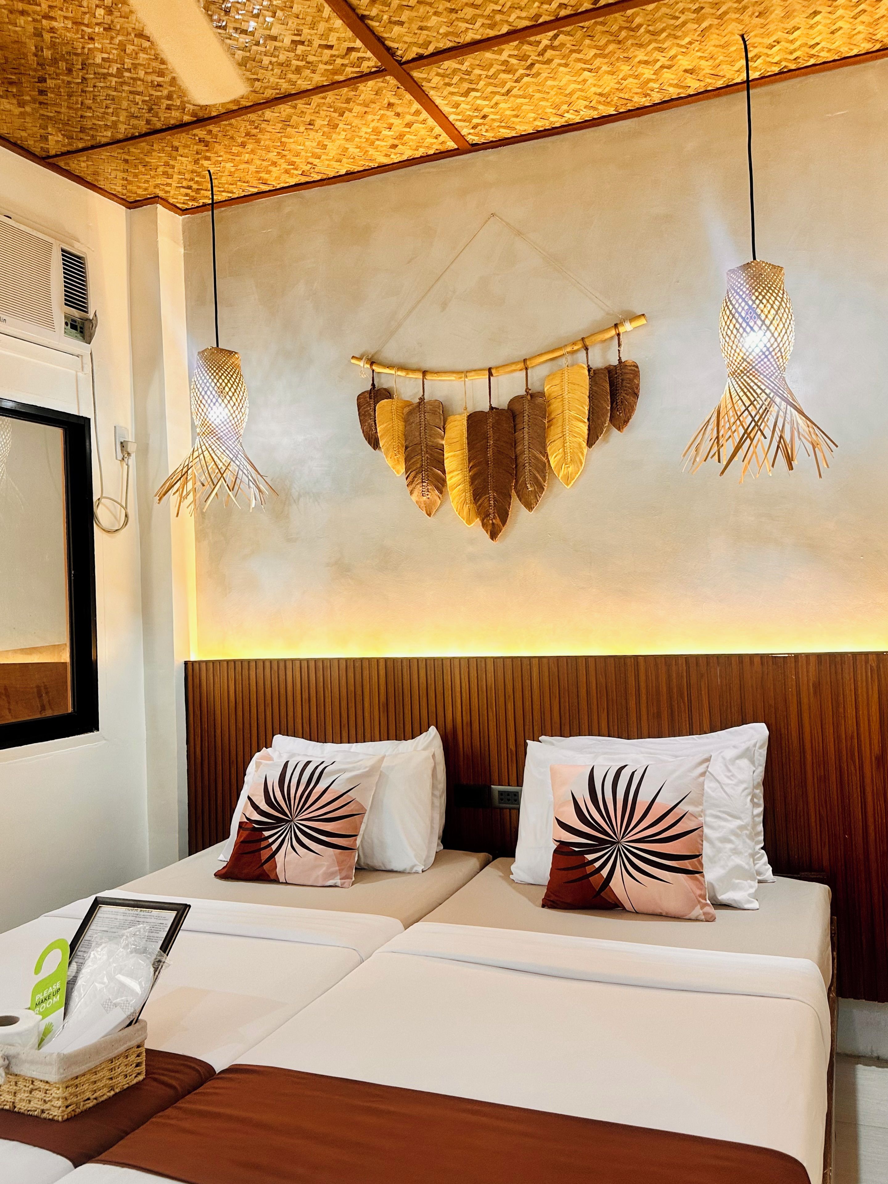 Une chambre d’hôtel avec un lit, deux oreillers ornés d’un motif de feuilles, un luminaire fixé au mur et un plafond en osier.