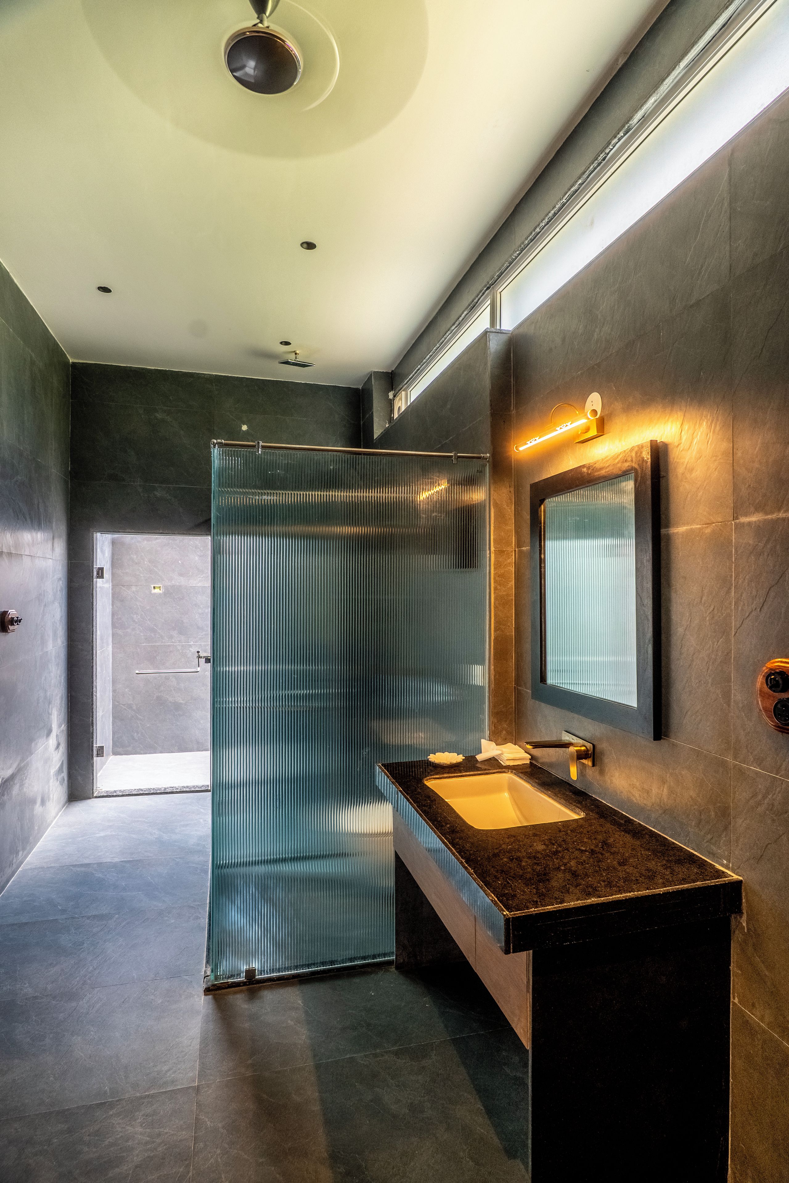 A modern bathroom with a glass shower enclosure, a sink with a dark countertop, and a mirror with a light fixture above it.
