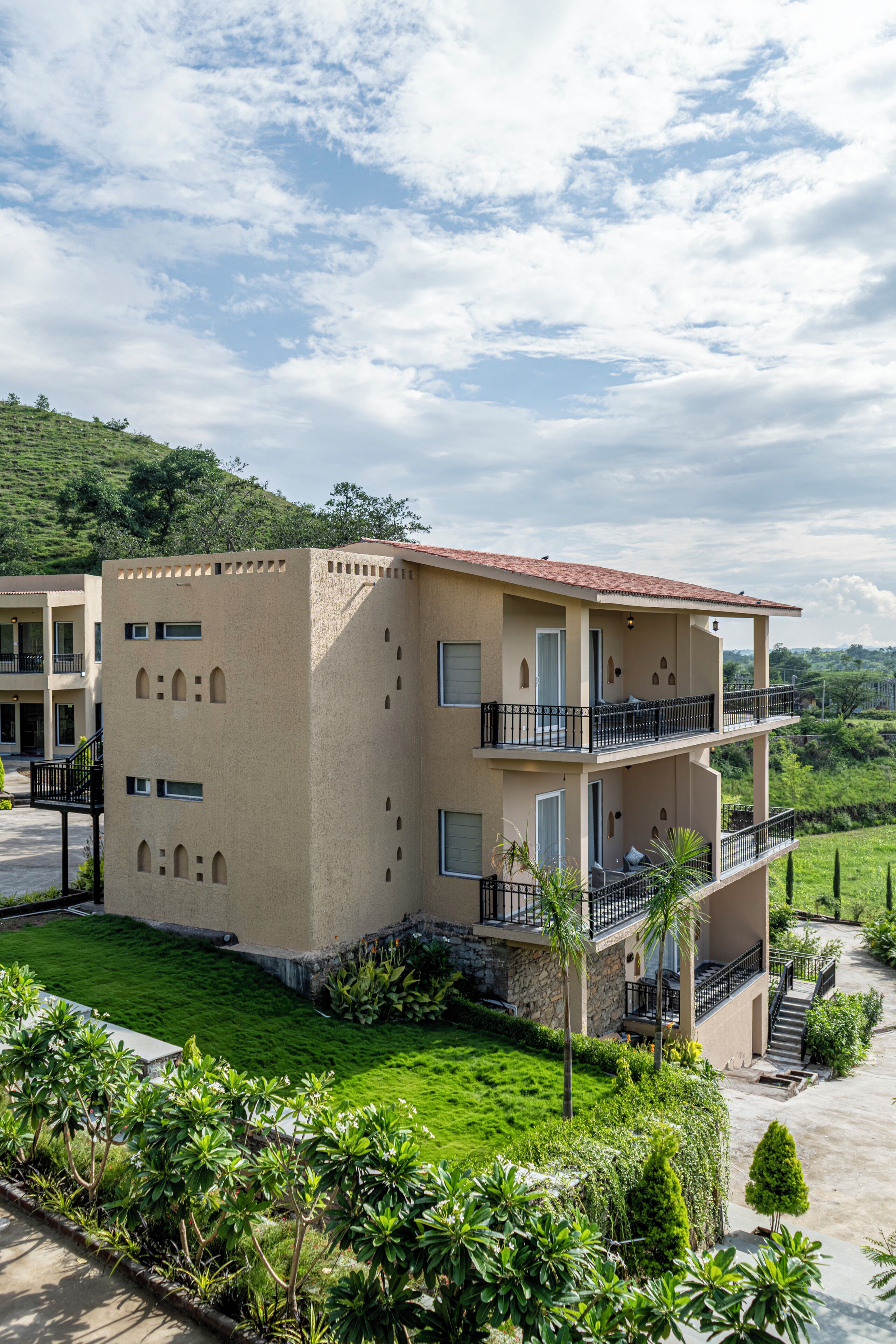 Un edificio de varios pisos con balcones, techo plano y un paisaje verde circundante.