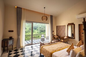 A bedroom with a large bed, a checkered floor, a balcony with a view of greenery, and a hanging light fixture.