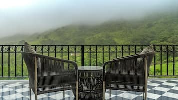 A balcony with two wicker chairs and a small round table, overlooking a lush green landscape with hills in the background.
