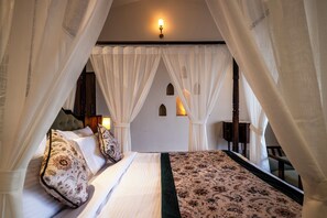 A bedroom with a canopy bed, a patterned bedspread, and a view of the night sky. - The Talhati (Kumbhalgarh)
