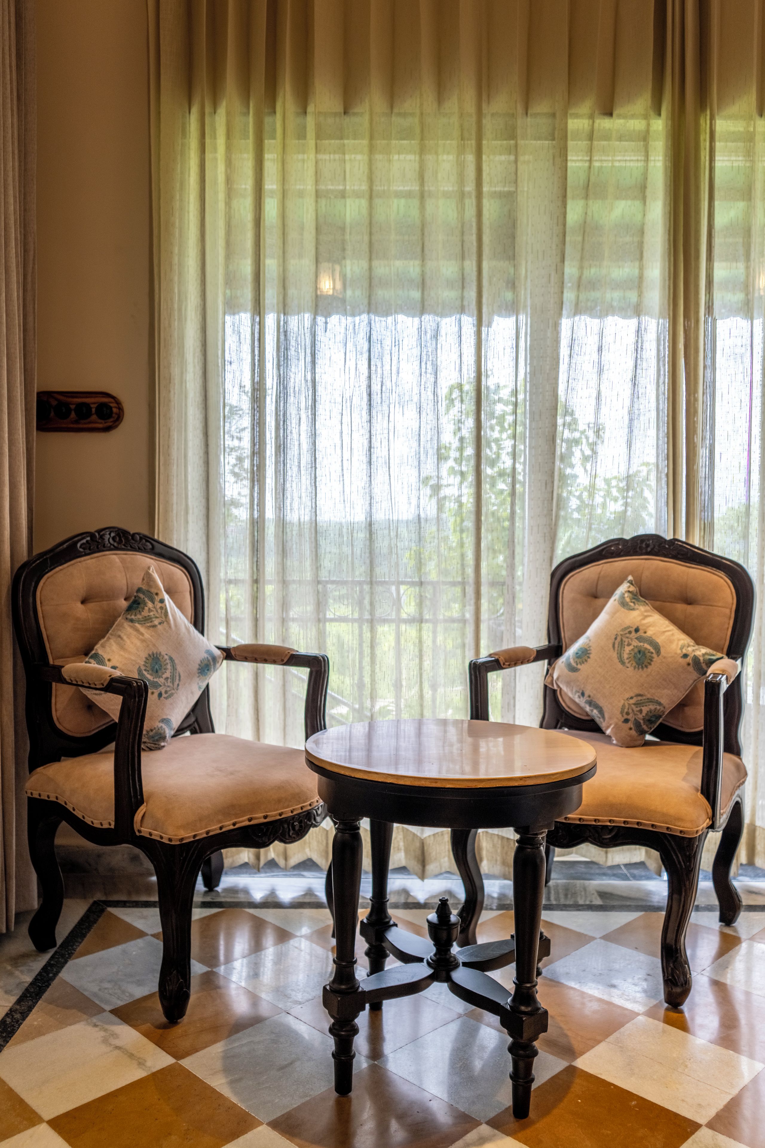 A room with two upholstered chairs with armrests, a small round table, and a checkered floor.