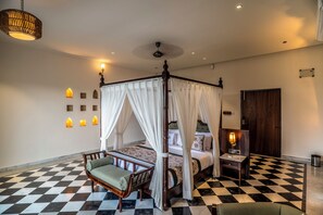 A four-poster canopy bed with a checkered floor, a small bedside table with a lamp, and wall sconces. - The Talhati (Kumbhalgarh)