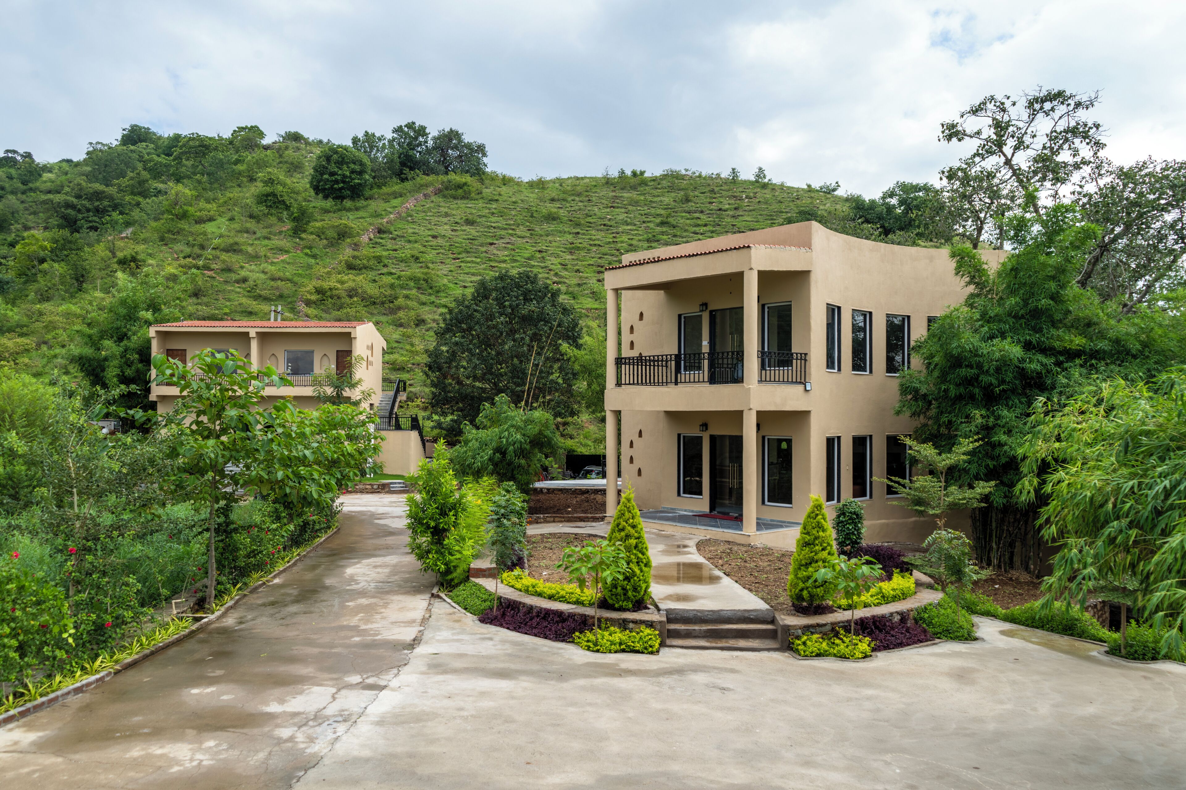 A two-story building with a balcony, surrounded by lush greenery and a hillside.