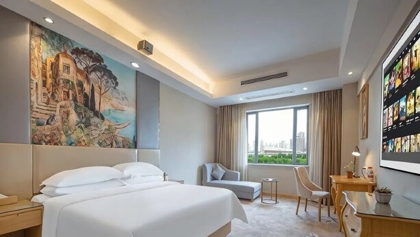 A hotel room with a large bed, a sofa, a small table, and a TV. - Vienna International Hotel (Changsha)