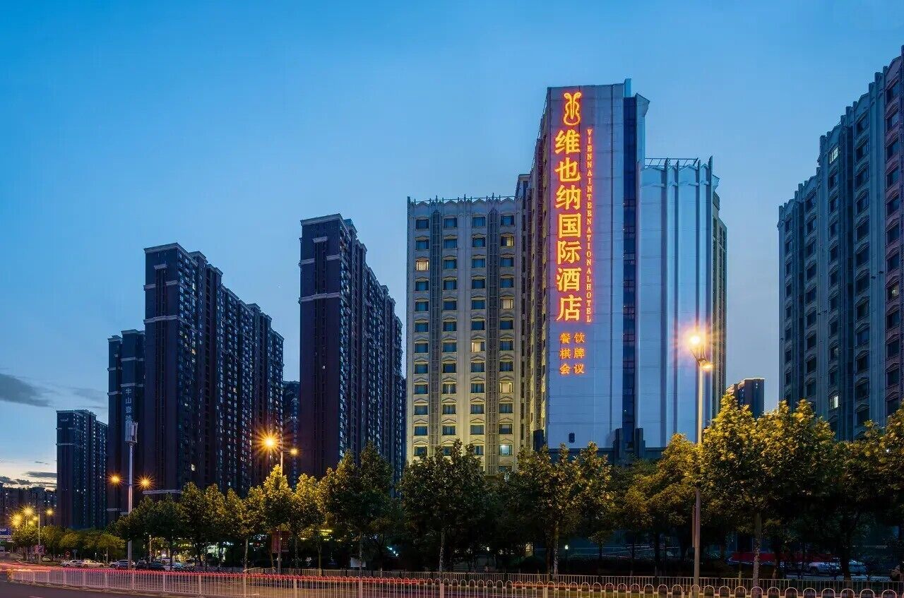 Un edificio de gran altura con señalización iluminada, rodeado de otros edificios altos y farolas.