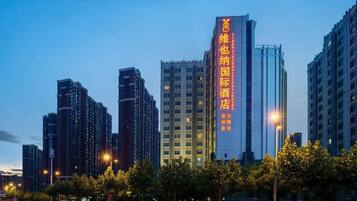 Un edificio de gran altura con señalización iluminada, rodeado de otros edificios altos y farolas.