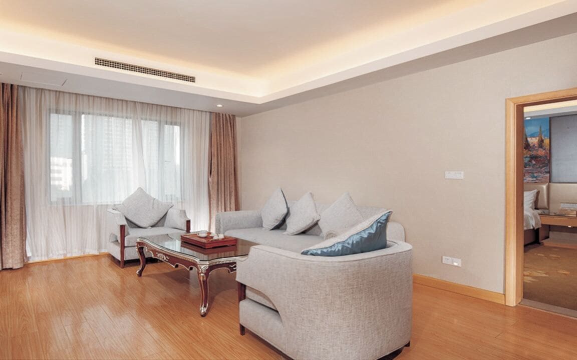 A modern living room with a sofa, a coffee table, and a large window with curtains.