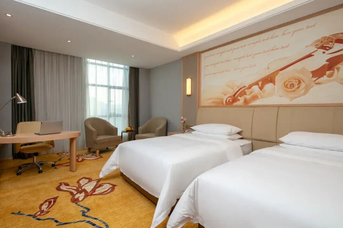 A hotel room with two beds, a desk with a laptop, a chair, and a large floral wall decoration.