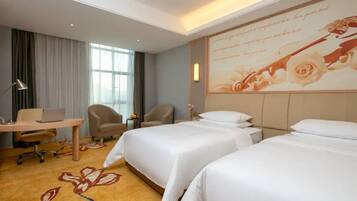 Quarto de hotel com duas camas, uma escrivaninha com um laptop, uma cadeira e uma grande decoração floral na parede.