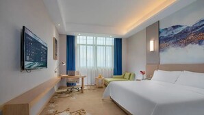 A hotel room with a bed, a desk, a chair, a TV, and a painting on the wall. - Vienna International Hotel (Changsha)