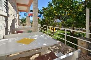 An outdoor seating area with a table and chairs, a white railing, and a view of a tree with fruit. - Laidback Apartments - One Bedroom Apartment With Balcony and Sea View (Orebic)