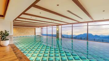 A spacious indoor swimming pool with a clear view of mountains through large windows.