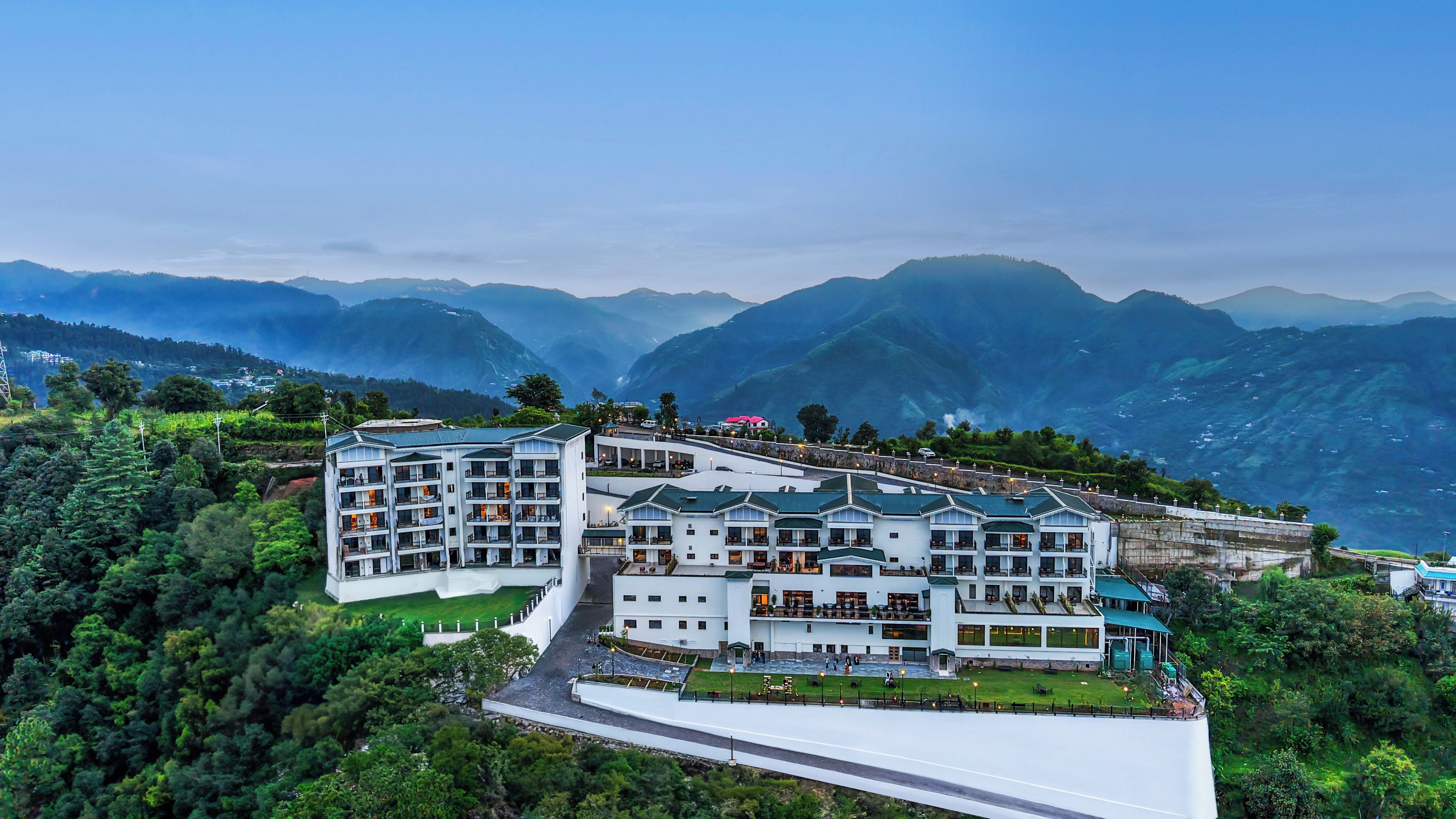 A multi-story hotel with a central courtyard, surrounded by lush greenery and mountains in the background.
