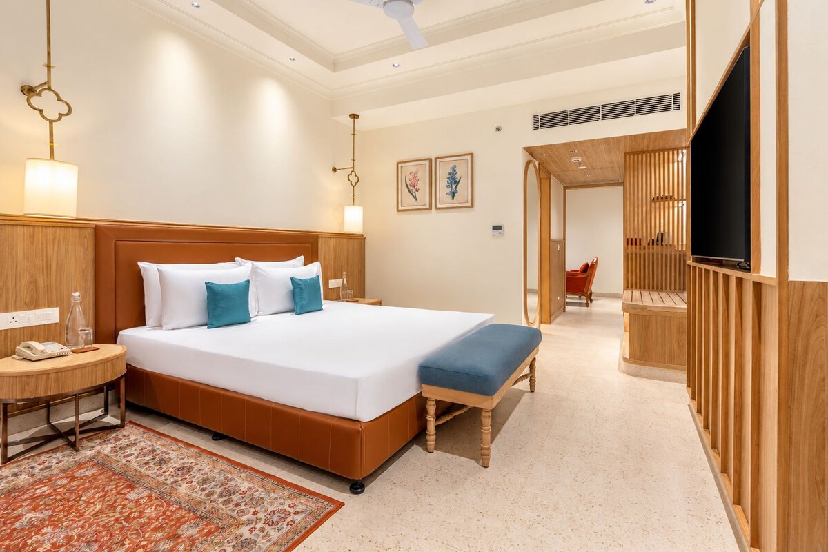 A hotel room with a large bed, bedside tables, a TV, and a wooden wardrobe.